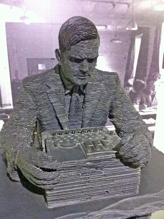 BletchleyPark_TNMOC 030.jpg - A sclupture of Turing made from slate. He looks down on an Enigma machine.